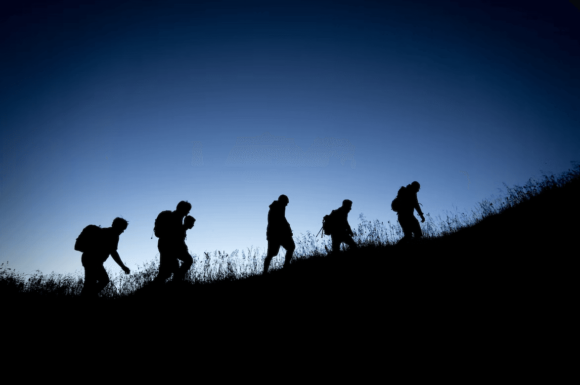 Silhouettes of hikers walking along a ridge against a blue sky.