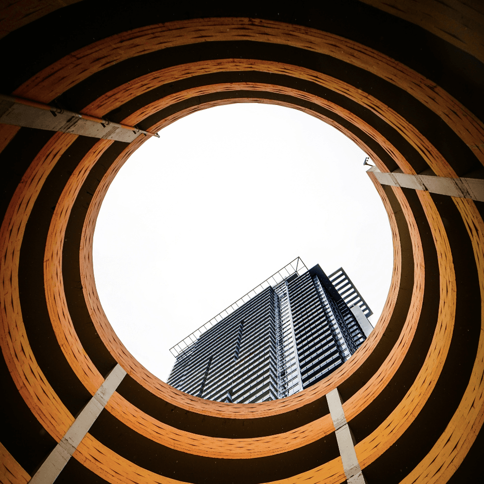 Looking up through a circular timber structure towards a tall building.